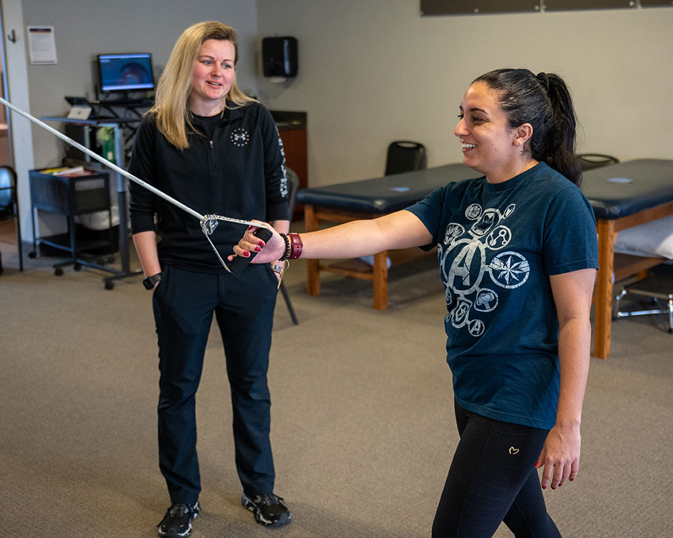 A physical therapist assistant smiles as she watches her patient stretch
