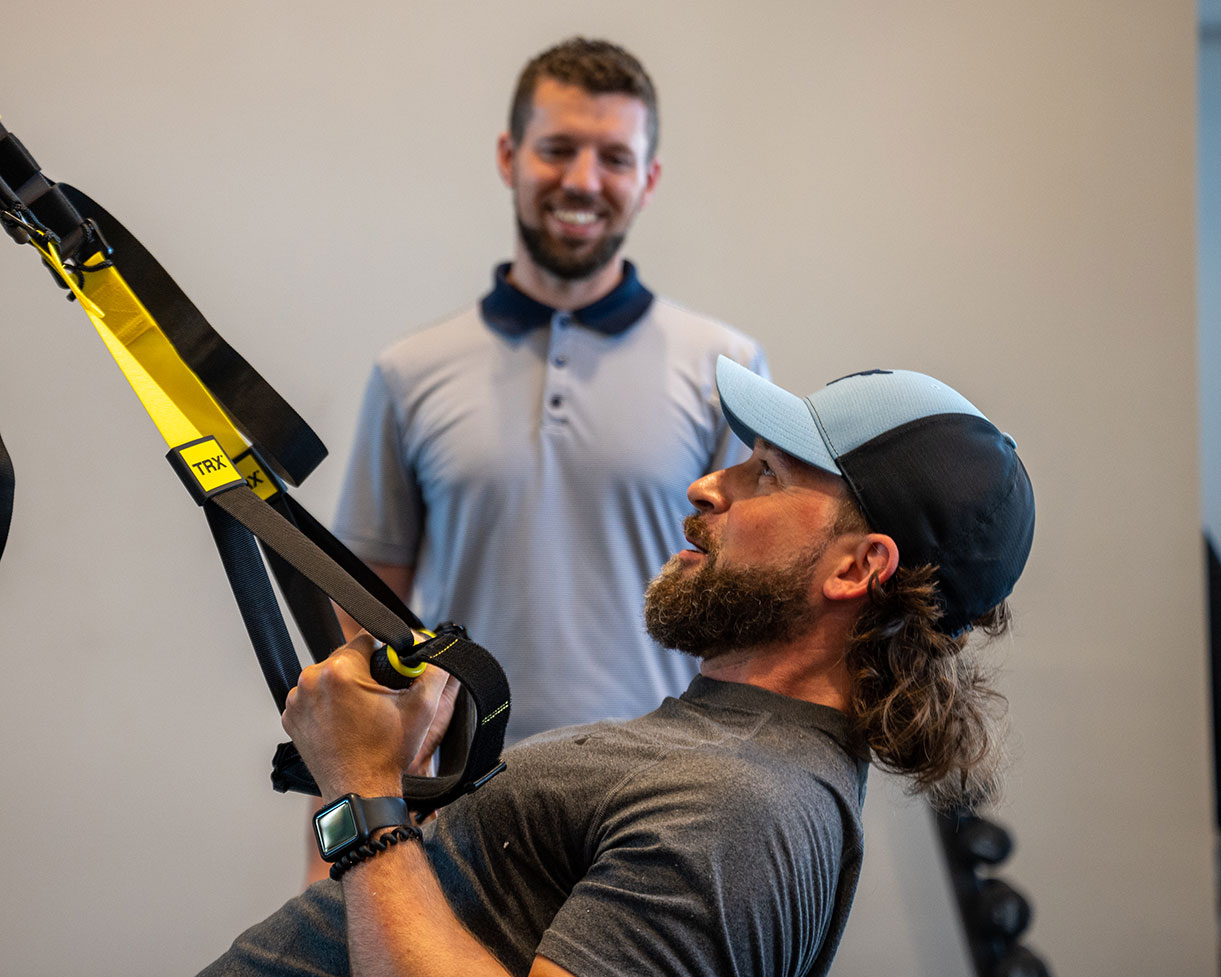 A physical therapist smiles as his patient pulls a resistance band.