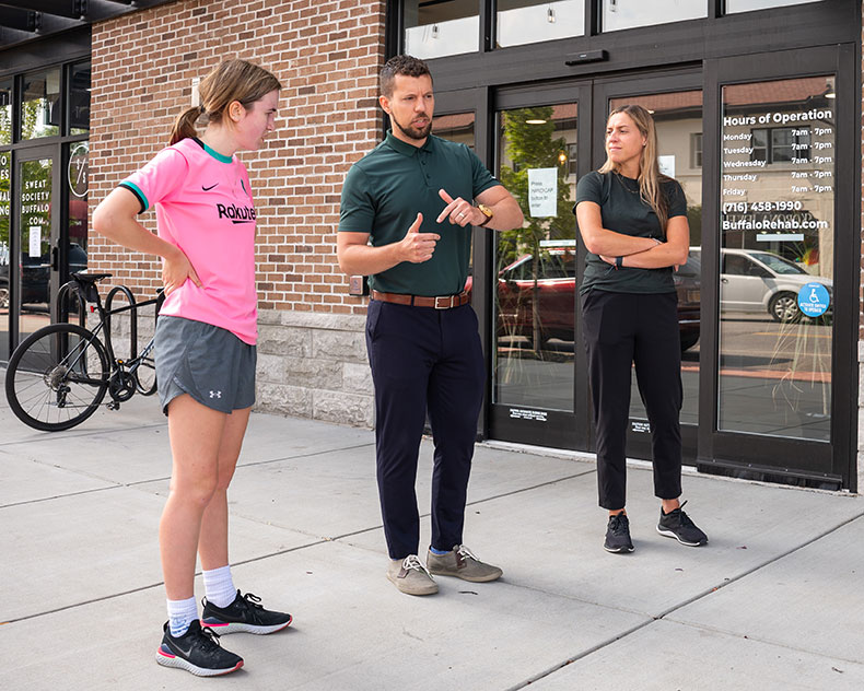 Two physical therapists smile as their patient prepares to run.