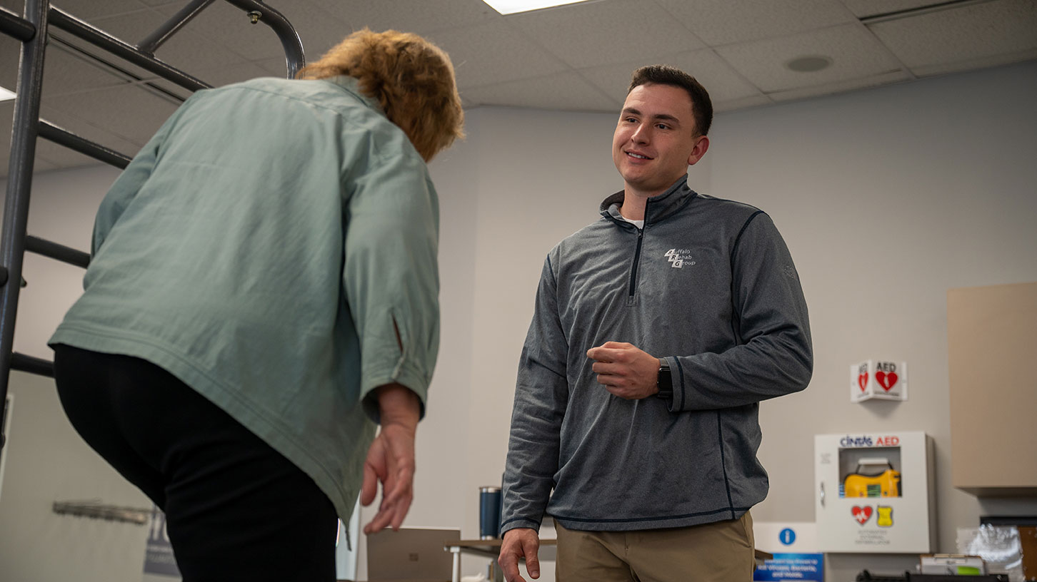 A physical therapist smiles as his patient walks toward him.