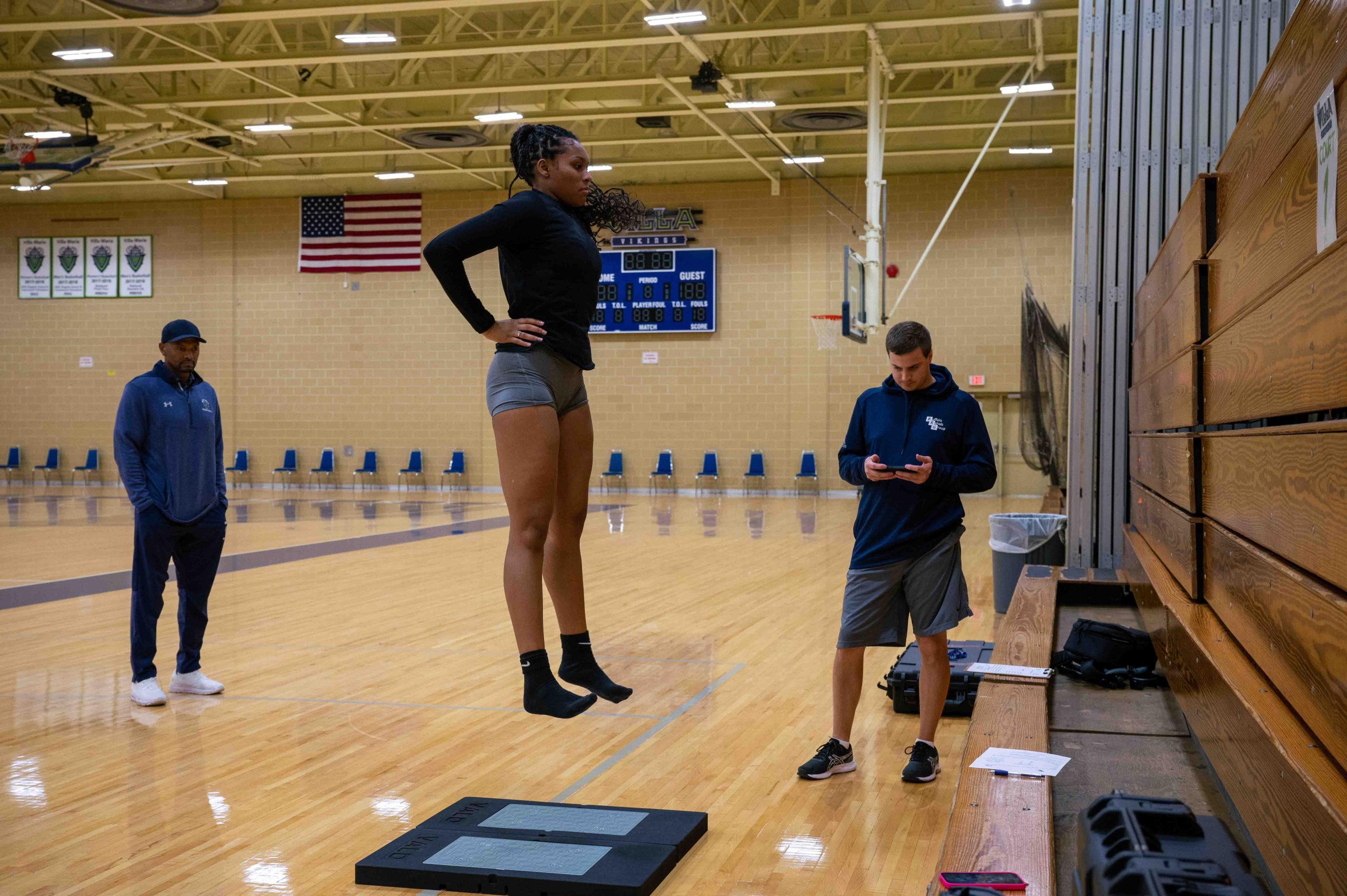 A physical therapist watches as his patient walks with a medicine ball.